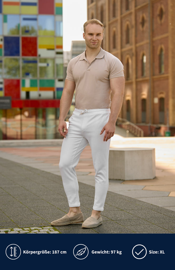 Model trägt ein beiges Slim Fit Poloshirt mit weißer Hose und steht vor mehreren Bürogebäuden.