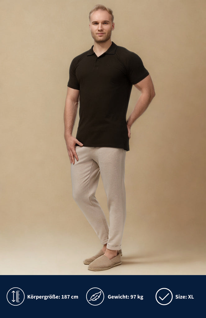 Model trägt ein schwarze Slim Fit Poloshirt in Muscle Fit Optik mit einer beigen Hose vor einen beigen Hintergrund.